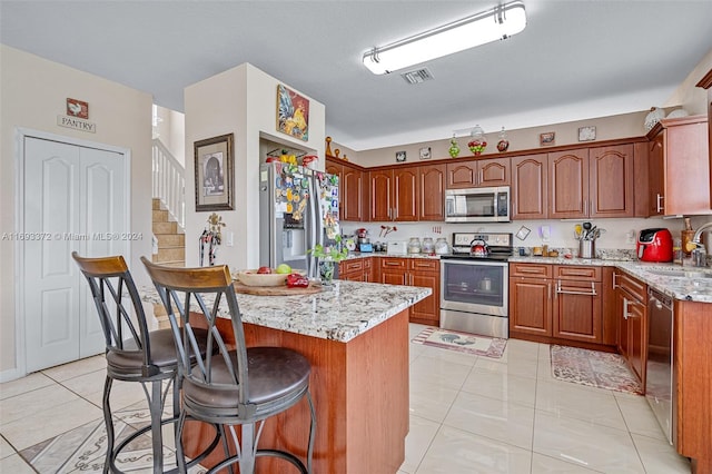 kitchen with stainless steel appliances, a center island, light tile patterned floors, sink, and light stone countertops