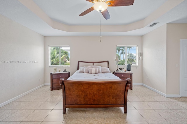 tiled bedroom featuring a tray ceiling, multiple windows, and ceiling fan