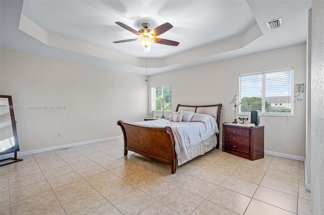 tiled bedroom featuring ceiling fan, multiple windows, and a raised ceiling