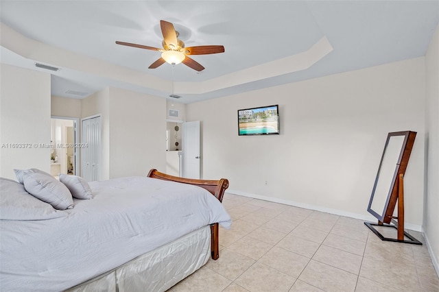 bedroom with a closet, light tile patterned flooring, ensuite bath, a raised ceiling, and ceiling fan