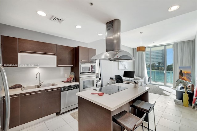 kitchen featuring island range hood, appliances with stainless steel finishes, a kitchen bar, hanging light fixtures, and sink