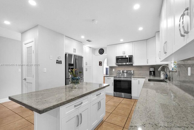 kitchen with white cabinets, appliances with stainless steel finishes, decorative backsplash, sink, and light stone counters