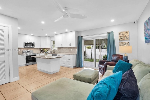 kitchen featuring backsplash, a kitchen island, light tile patterned flooring, white cabinetry, and stainless steel appliances