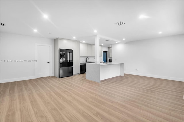 kitchen with black appliances, a kitchen bar, white cabinetry, sink, and light hardwood / wood-style flooring