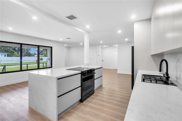 kitchen featuring black electric range, sink, white cabinetry, a kitchen island, and light hardwood / wood-style floors