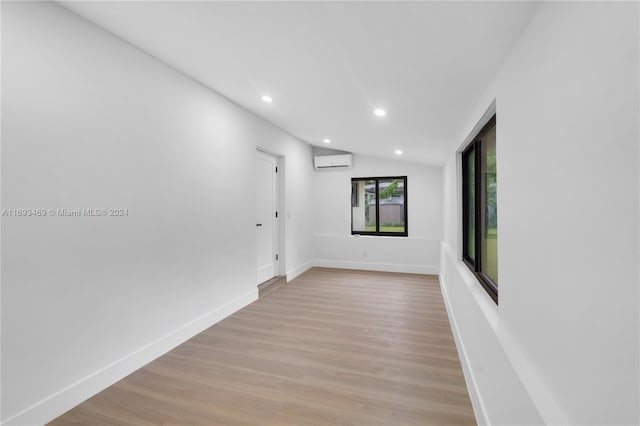 unfurnished room with light hardwood / wood-style floors, lofted ceiling, and a wall mounted AC