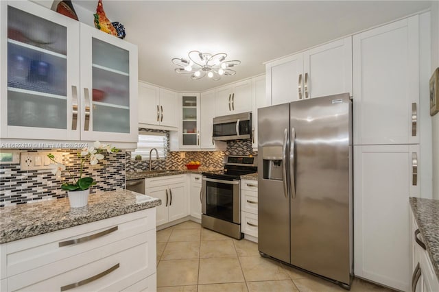 kitchen featuring backsplash, white cabinets, light tile patterned flooring, light stone counters, and stainless steel appliances