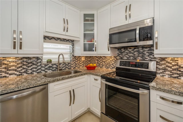 kitchen with appliances with stainless steel finishes, tasteful backsplash, light stone counters, sink, and white cabinets