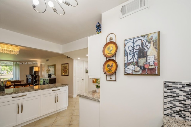 kitchen with an inviting chandelier, white cabinets, light tile patterned floors, tasteful backsplash, and stone countertops