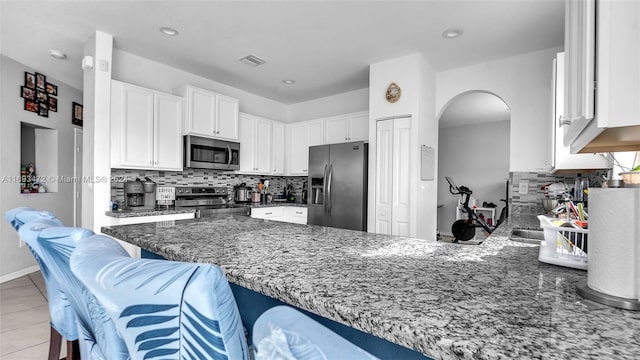 kitchen with a kitchen bar, appliances with stainless steel finishes, kitchen peninsula, and dark stone countertops