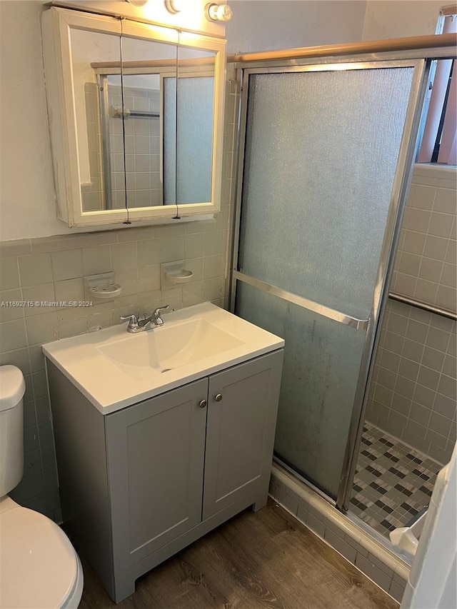 bathroom with hardwood / wood-style floors, a shower with door, and tile walls