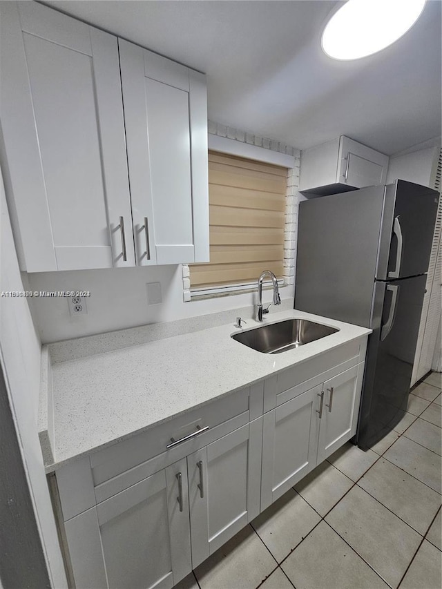 kitchen featuring white cabinets, light tile patterned flooring, stainless steel refrigerator, and sink