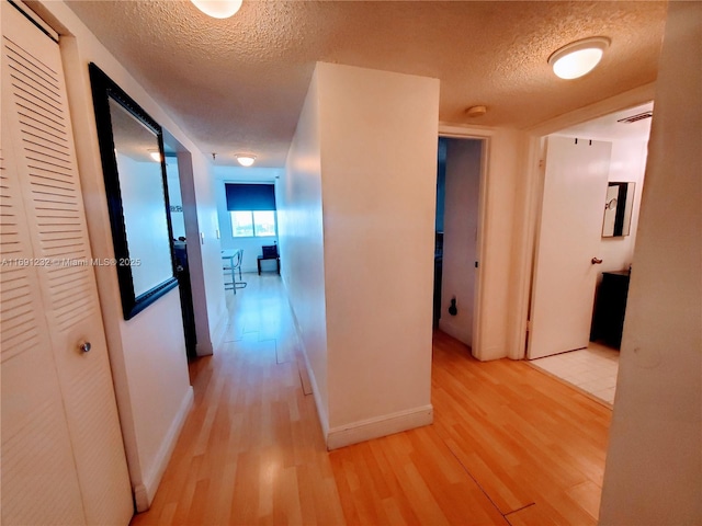 corridor with a textured ceiling and light wood-type flooring