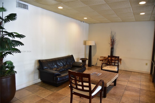 living room with a drop ceiling and light tile patterned flooring