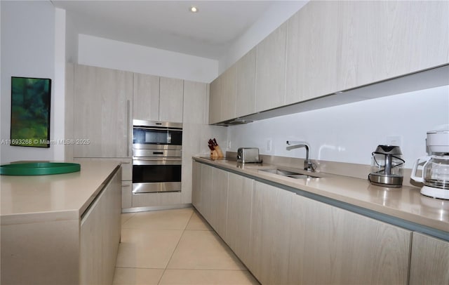 kitchen with modern cabinets, light countertops, double oven, a sink, and light tile patterned flooring