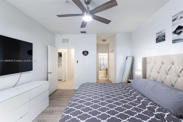 bedroom with washer / dryer, ensuite bath, light hardwood / wood-style flooring, and ceiling fan