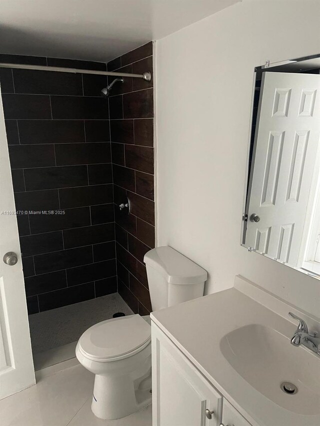 bathroom featuring toilet, tile patterned flooring, vanity, and tiled shower