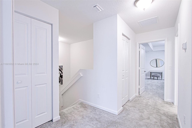 hall with light colored carpet and a textured ceiling