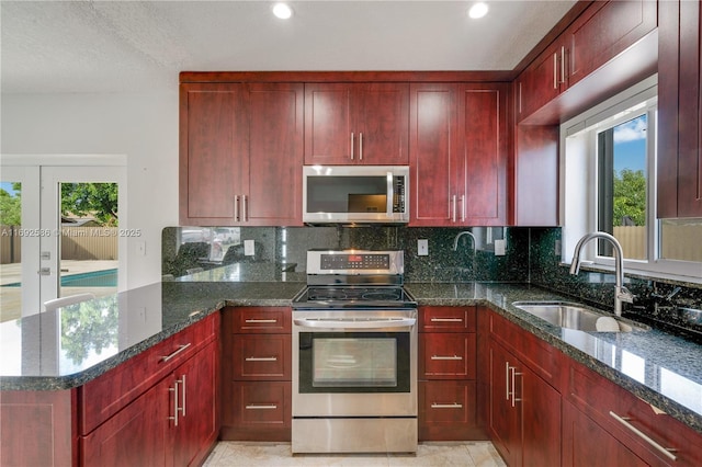 kitchen featuring sink, dark stone counters, decorative backsplash, light tile patterned floors, and appliances with stainless steel finishes