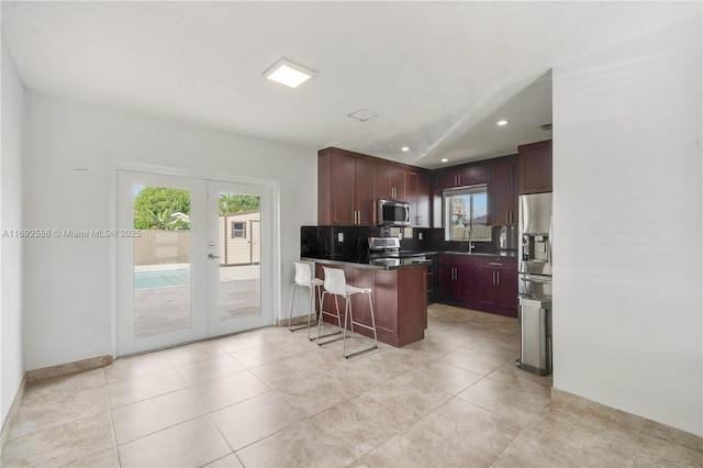 kitchen with a peninsula, appliances with stainless steel finishes, french doors, backsplash, and dark countertops