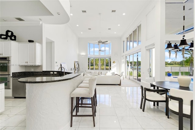 kitchen with stainless steel appliances, pendant lighting, white cabinets, ceiling fan with notable chandelier, and ornamental molding