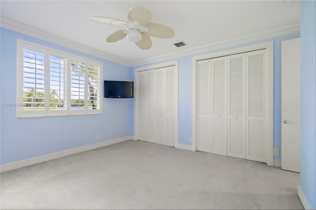 unfurnished bedroom featuring two closets, ceiling fan, crown molding, and light colored carpet