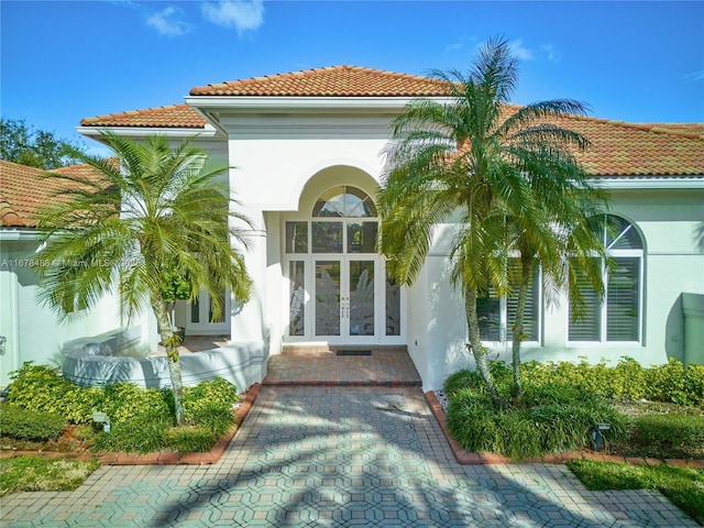 entrance to property featuring a tiled roof, stucco siding, and french doors