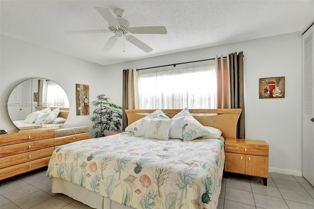 bedroom featuring a closet, ceiling fan, light tile patterned flooring, and a textured ceiling