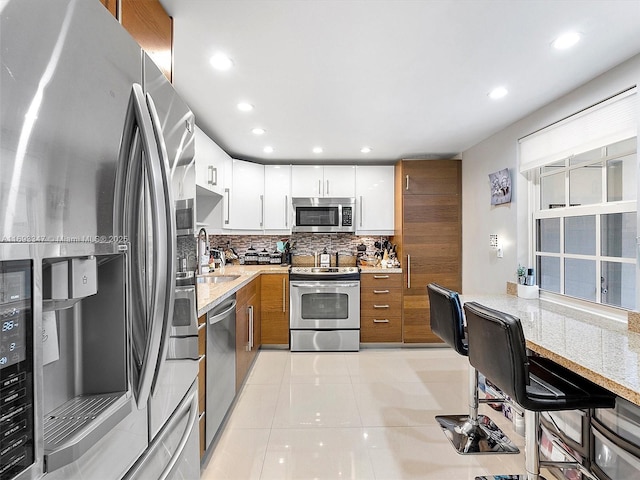 kitchen with sink, light tile patterned flooring, stainless steel appliances, white cabinets, and light stone countertops