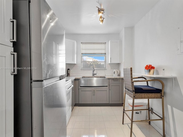 kitchen featuring white cabinetry, sink, backsplash, light stone counters, and stainless steel fridge