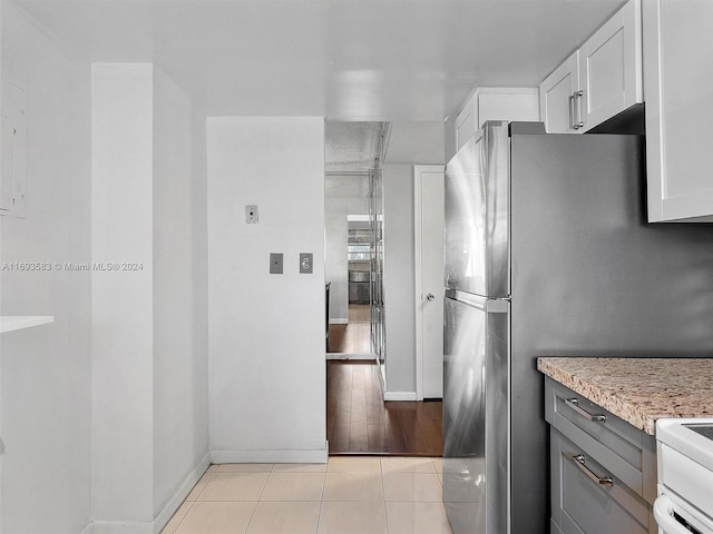 kitchen with white range oven, stainless steel refrigerator, white cabinetry, and light tile patterned flooring