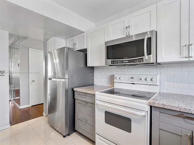 kitchen with white cabinetry, light tile patterned flooring, appliances with stainless steel finishes, backsplash, and light stone countertops