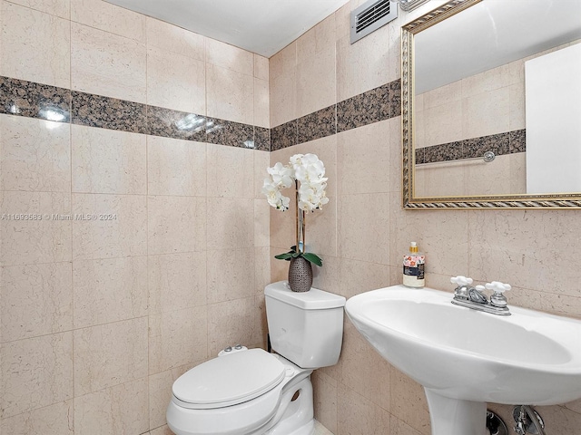 bathroom with toilet, tile walls, and sink