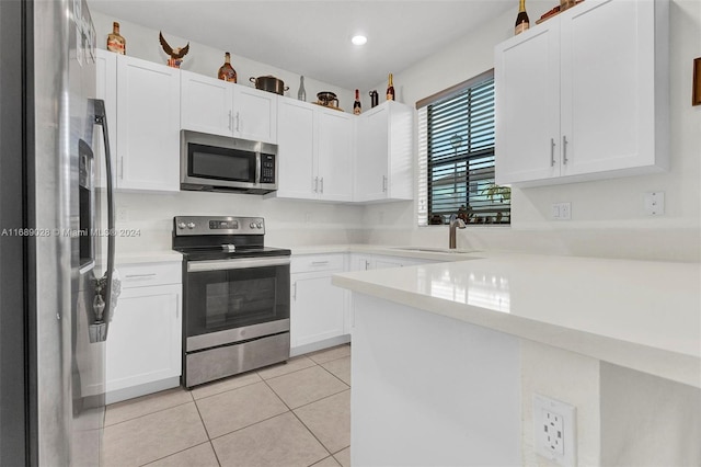 kitchen with sink, light tile patterned floors, appliances with stainless steel finishes, white cabinetry, and kitchen peninsula