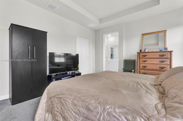 bedroom featuring a raised ceiling, ensuite bath, and carpet