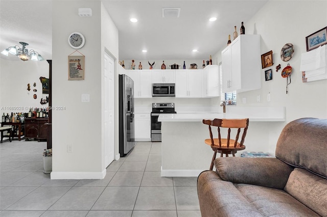 kitchen with stainless steel appliances, light tile patterned floors, kitchen peninsula, a kitchen bar, and white cabinets