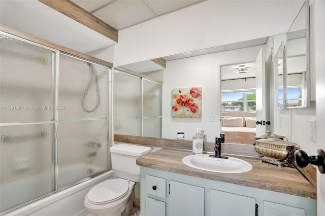 full bathroom featuring shower / bath combination with glass door, vanity, toilet, and a drop ceiling