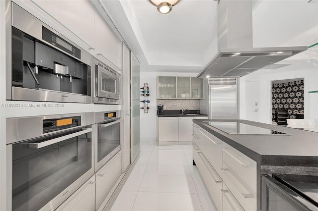 18201 Collins Ave Unit 1002, Sunny Isles Beach, FL 33160 - kitchen with island exhaust hood, built in appliances, dark countertops, and light tile patterned flooring