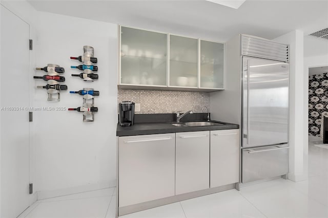 18201 Collins Ave Unit 1002, Sunny Isles Beach, FL 33160 - kitchen featuring built in fridge, dark countertops, tasteful backsplash, glass insert cabinets, and white cabinetry