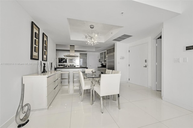 dining space with a raised ceiling, light tile patterned floors, and a chandelier