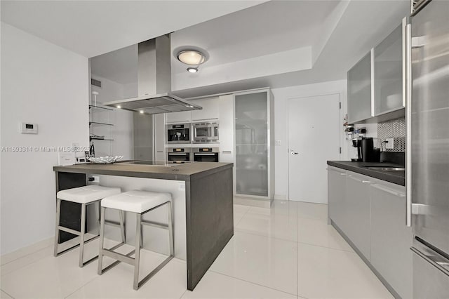 kitchen featuring kitchen peninsula, a breakfast bar area, island range hood, light tile patterned floors, and appliances with stainless steel finishes