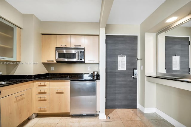 kitchen featuring light brown cabinetry, dark stone countertops, and sink