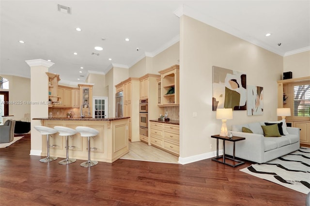 kitchen with ornamental molding, a kitchen bar, light hardwood / wood-style floors, kitchen peninsula, and backsplash