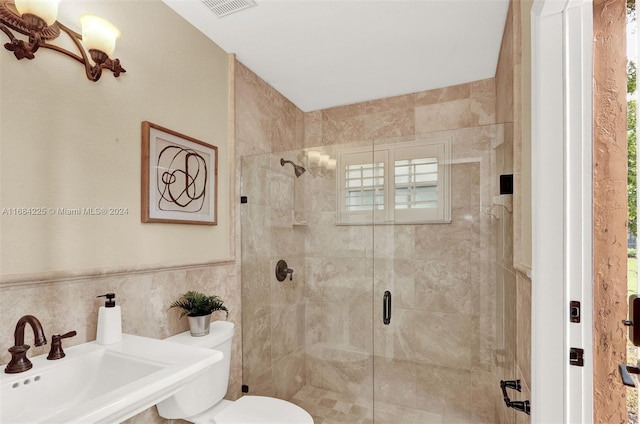 bathroom with toilet, a shower with shower door, tile walls, and sink