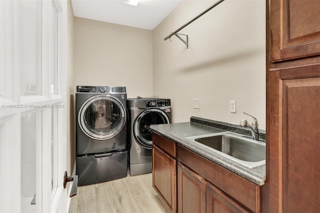 laundry room with washing machine and clothes dryer, sink, cabinets, and light hardwood / wood-style flooring