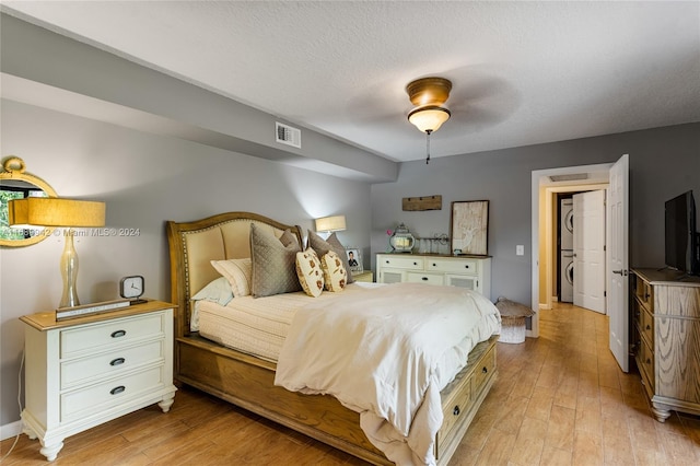 bedroom with a textured ceiling, light wood-type flooring, ceiling fan, and stacked washer / drying machine