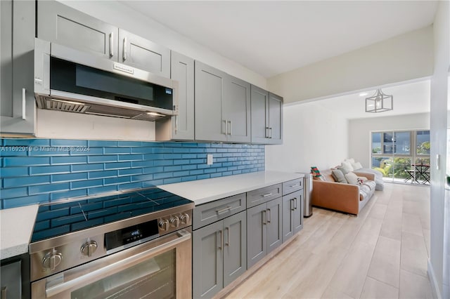 kitchen with gray cabinets, backsplash, appliances with stainless steel finishes, and decorative light fixtures