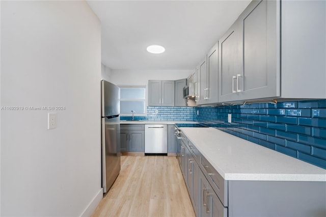 kitchen with appliances with stainless steel finishes, light wood-type flooring, tasteful backsplash, gray cabinetry, and sink