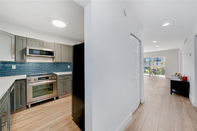 kitchen with gray cabinetry, decorative backsplash, light hardwood / wood-style flooring, and appliances with stainless steel finishes