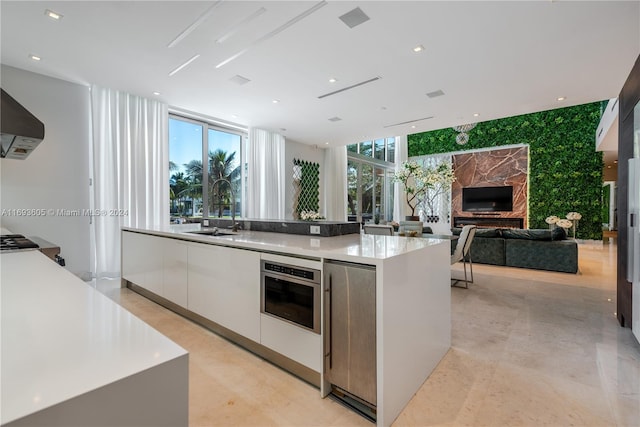 kitchen featuring white cabinetry, stainless steel oven, sink, a fireplace, and a center island with sink